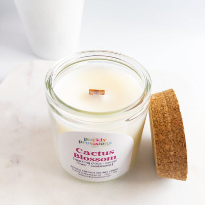 Candle in a glass jar with a cork lid on a white surface, featuring a label with text.