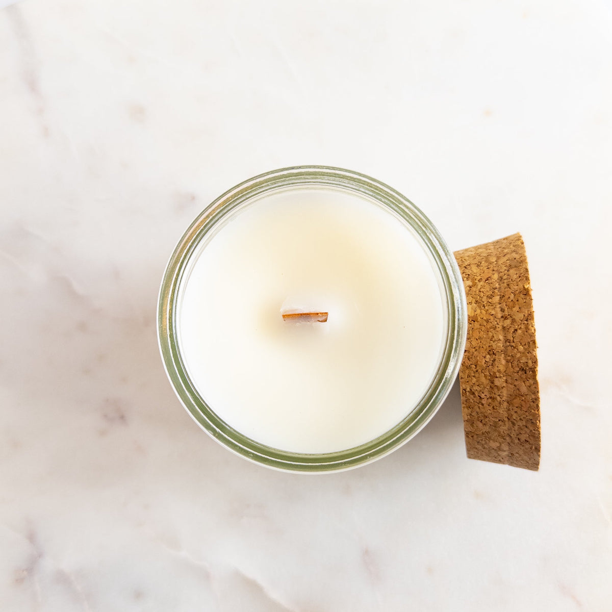 Candle in a glass jar with a cork lid on a marble surface