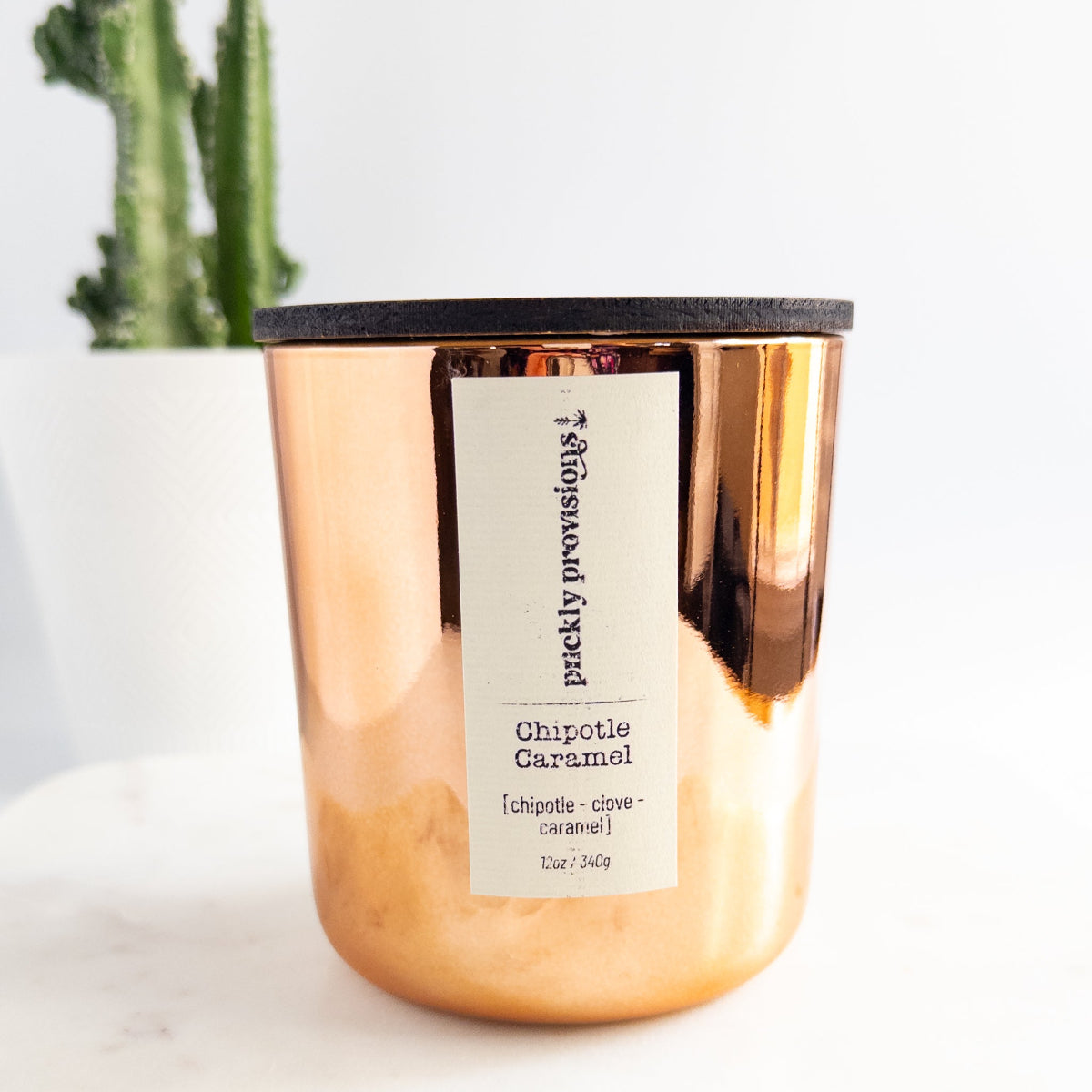 Rose gold copper candle with a label on a white surface, cactus in the background