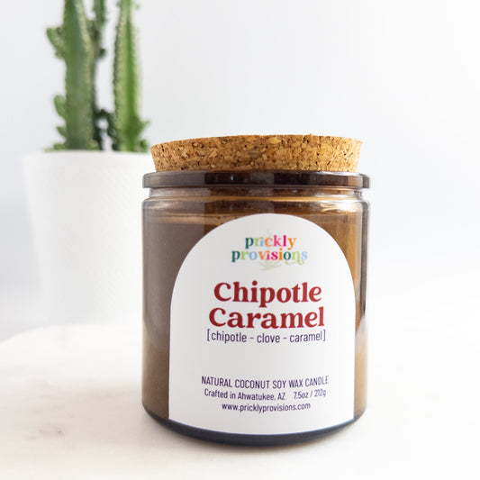 Candle jar labeled 'Chipotle Caramel' by Prickly Provisions on a white surface with a cactus in the background.