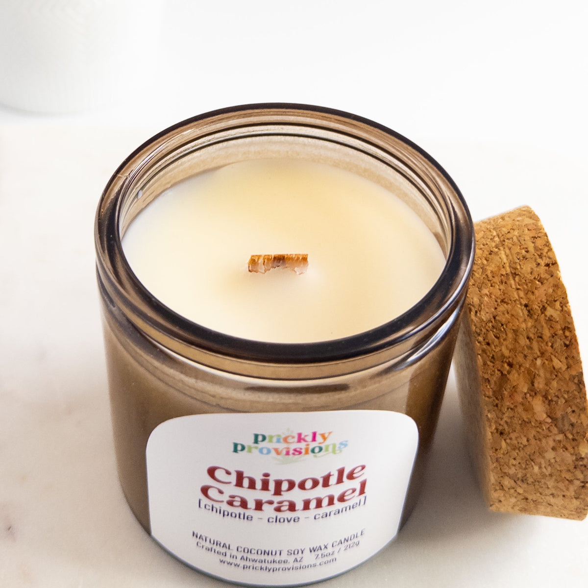 Candle in a glass jar labeled 'Chipotle Caramel' with a cork lid on a white background