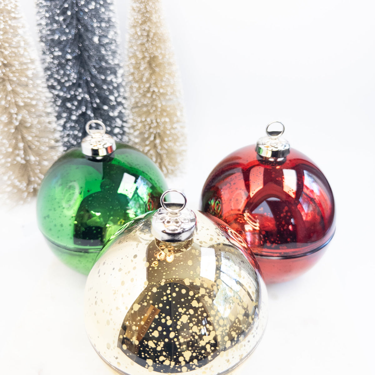 Three colorful glass ornament candles with a glittery background