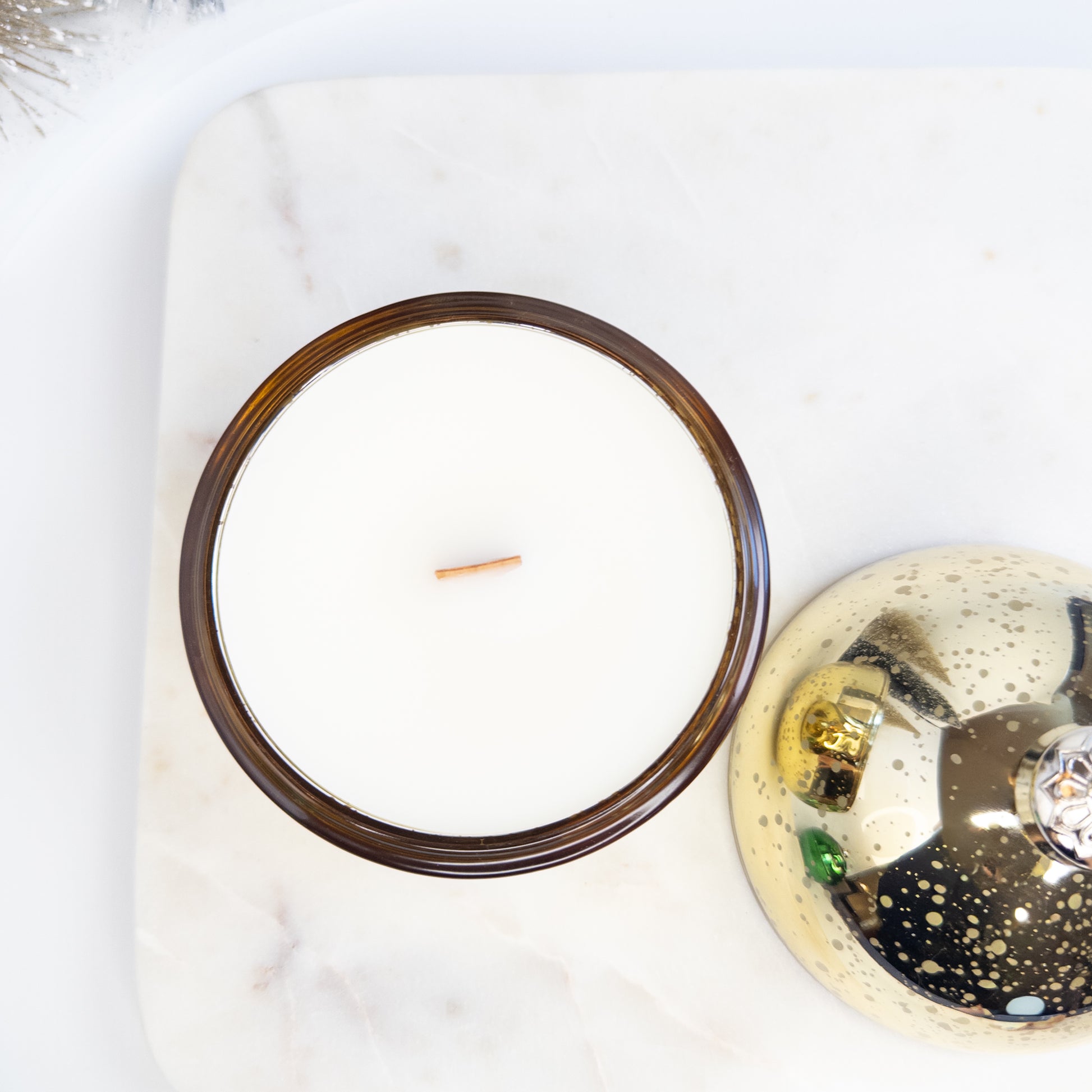 Gold Christmas ornament candle with wooden wick on a white surface