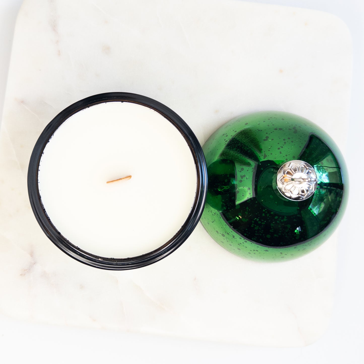 Green glass ornament candle with a wooden wick on a white marble surface