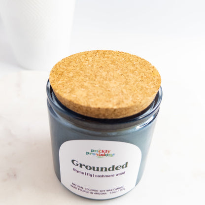 Jar candle with a cork lid labeled 'Grounded' on a white background