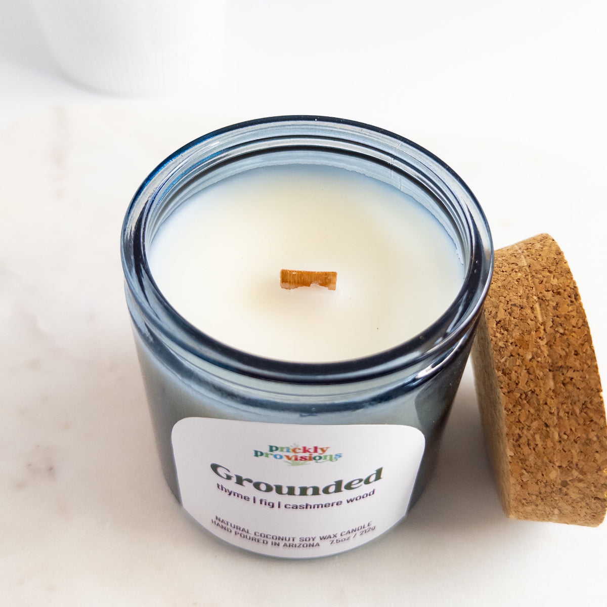 Candle in a glass jar labeled 'Grounded' with a cork lid on a light background