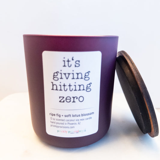 It’s Giving Hitting Zero 12 oz wood-wick candle in a matte plum glass vessel.