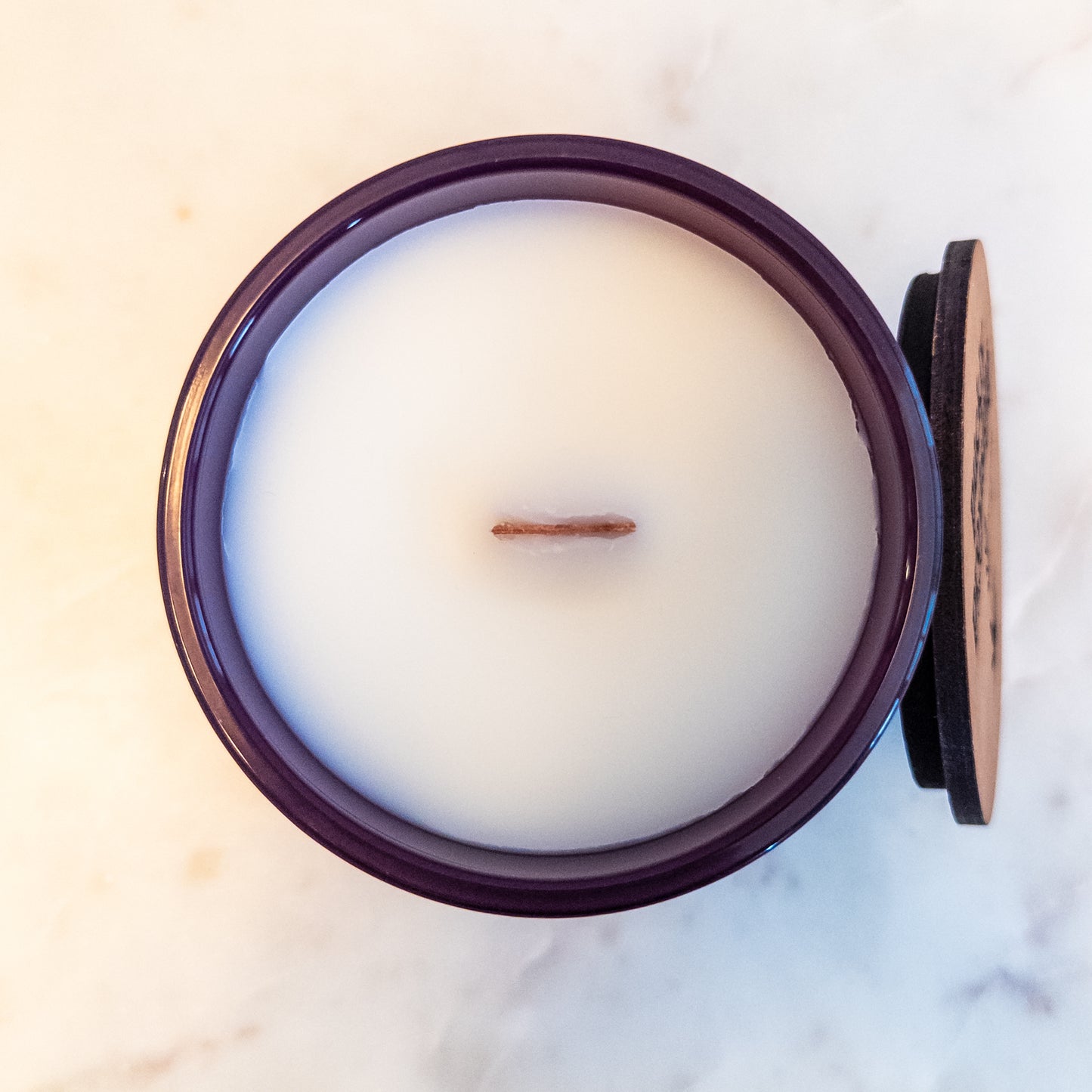 Candle in a matte plum jar with a wooden wick on a marble surface