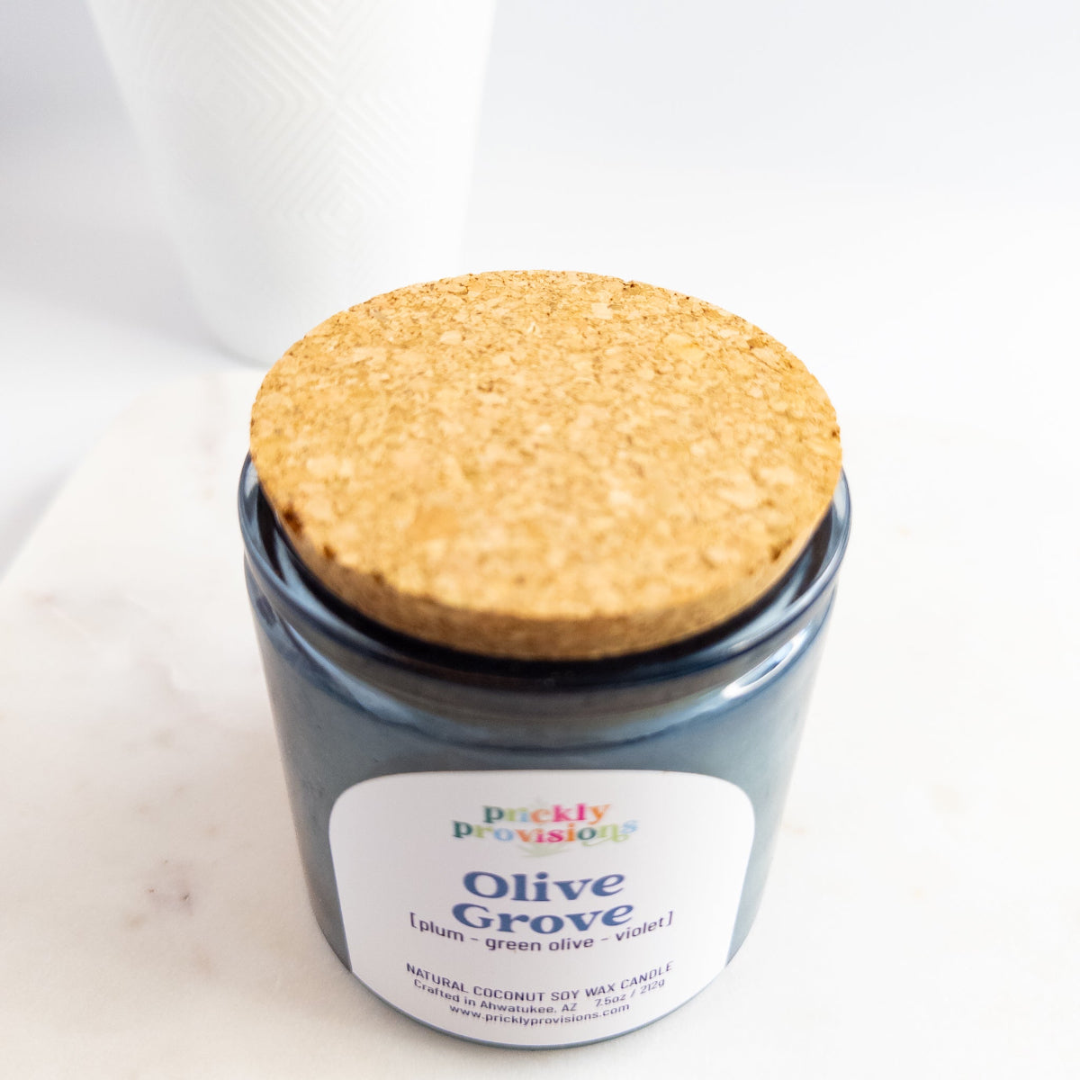 Jar of candle labeled 'Olive Grove' with a cork lid on a white background