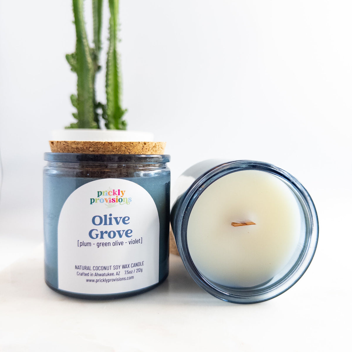 Candle jar labeled 'Olive Grove' from Prickly Provisions with a plant in the background.