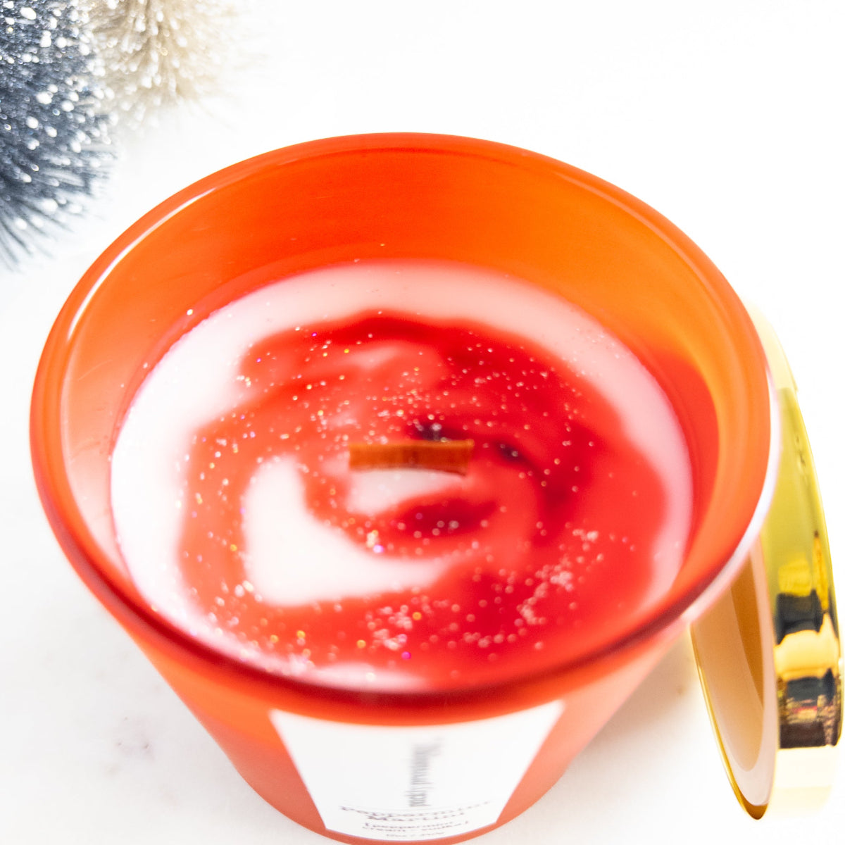 Candle in a red holder with a red and white swirl design on a white background