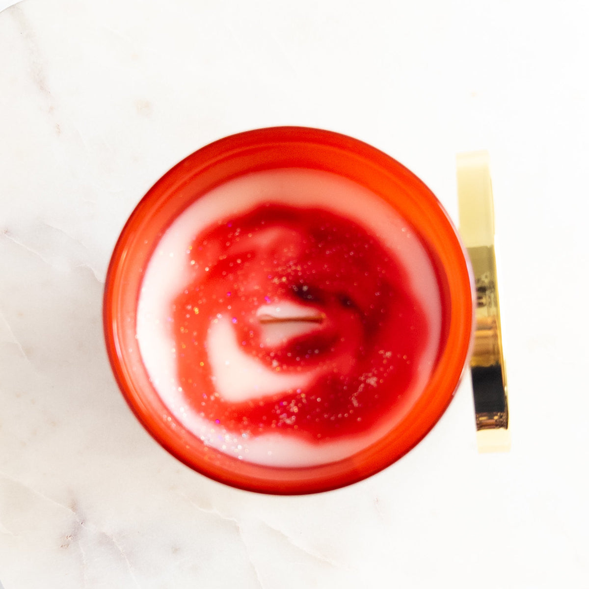 Red candle with a white swirl on a white marble surface