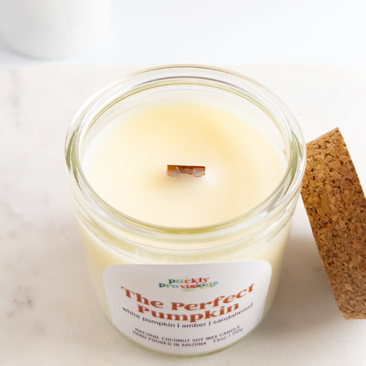 Candle in a glass jar labeled 'The Perfect Pumpkin' on a white surface.