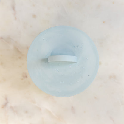 Light blue cement candle with lid on a marble surface