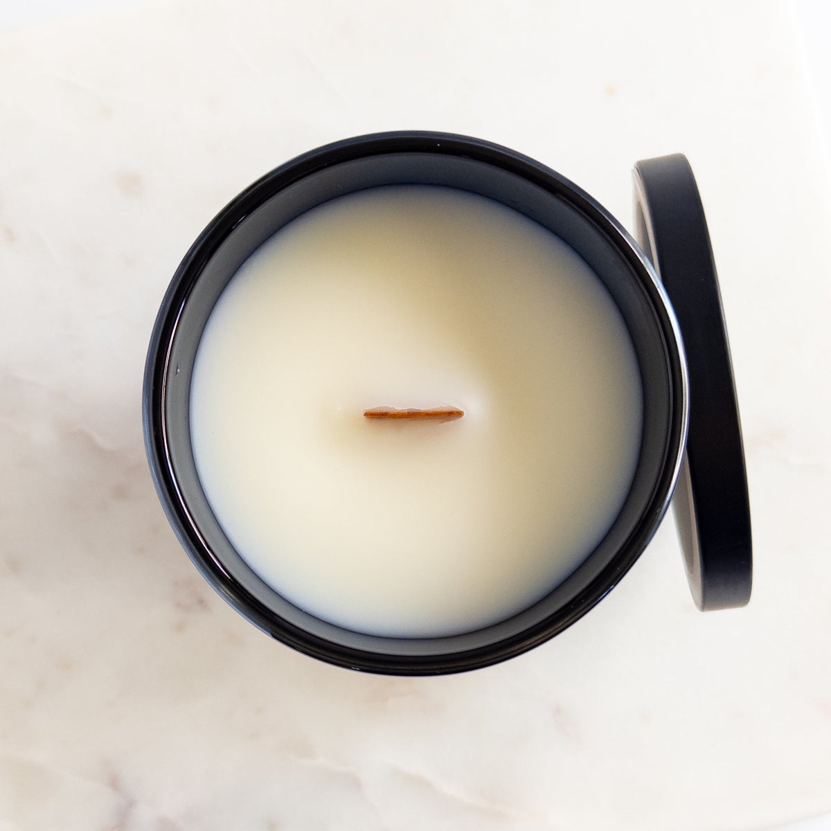 Candle in a black container with a white lid on a marble surface