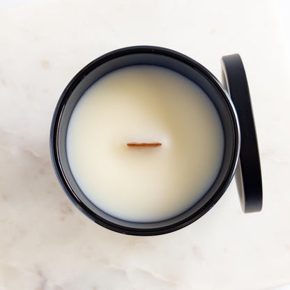 Candle in a black container with a white lid on a marble surface