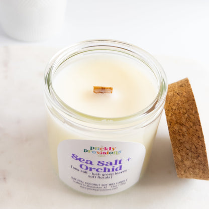 Candle in a glass jar labeled 'Sea Salt Orchid' with a wooden coaster on a white background
