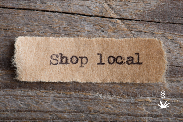 A rustic beige paper label with the words 'Shop local' printed in black typewriter-style font, placed on a weathered brown wooden surface.