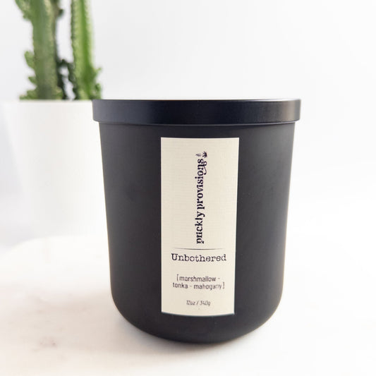 Black candle labeled 'Unbothered' with a cactus in the background