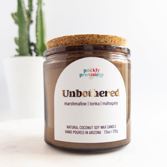 Candle jar labeled 'Unbothered' with a cork lid on a white background