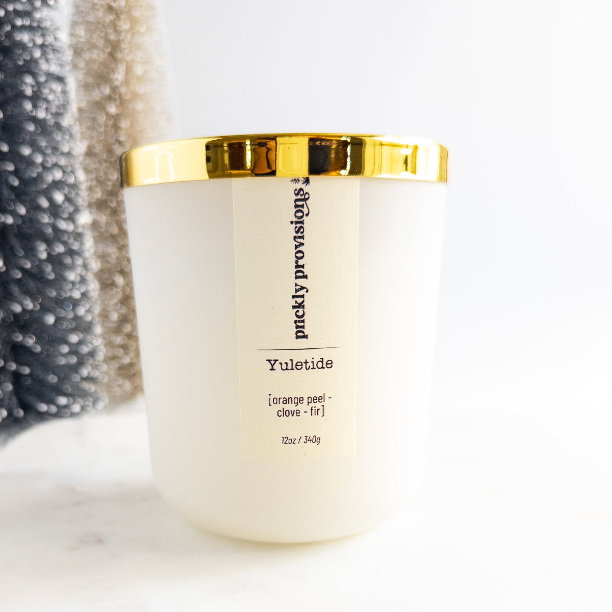 White candle with gold lid labeled 'Yuletide' by Puckity Provisions on a white background.