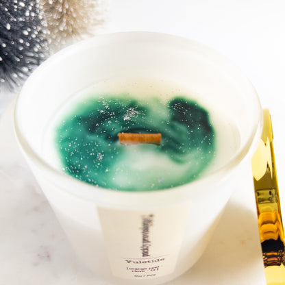 Candle with a green and white design inside, on a marble surface.